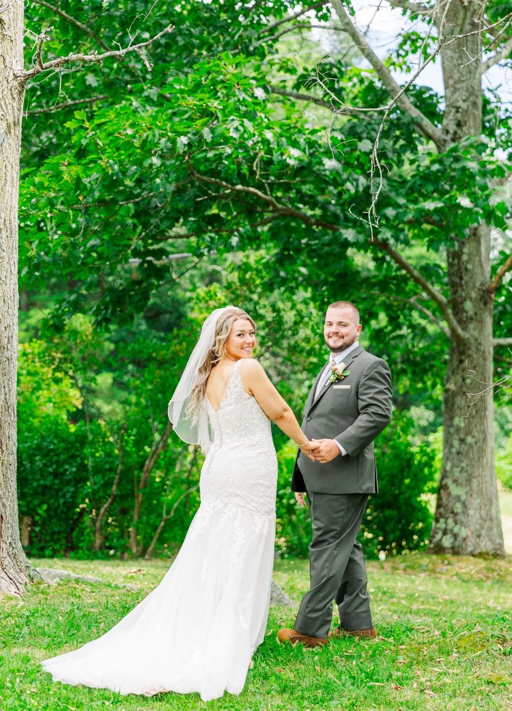 Wedding couple poses in natural outdoor setting with lush green trees.