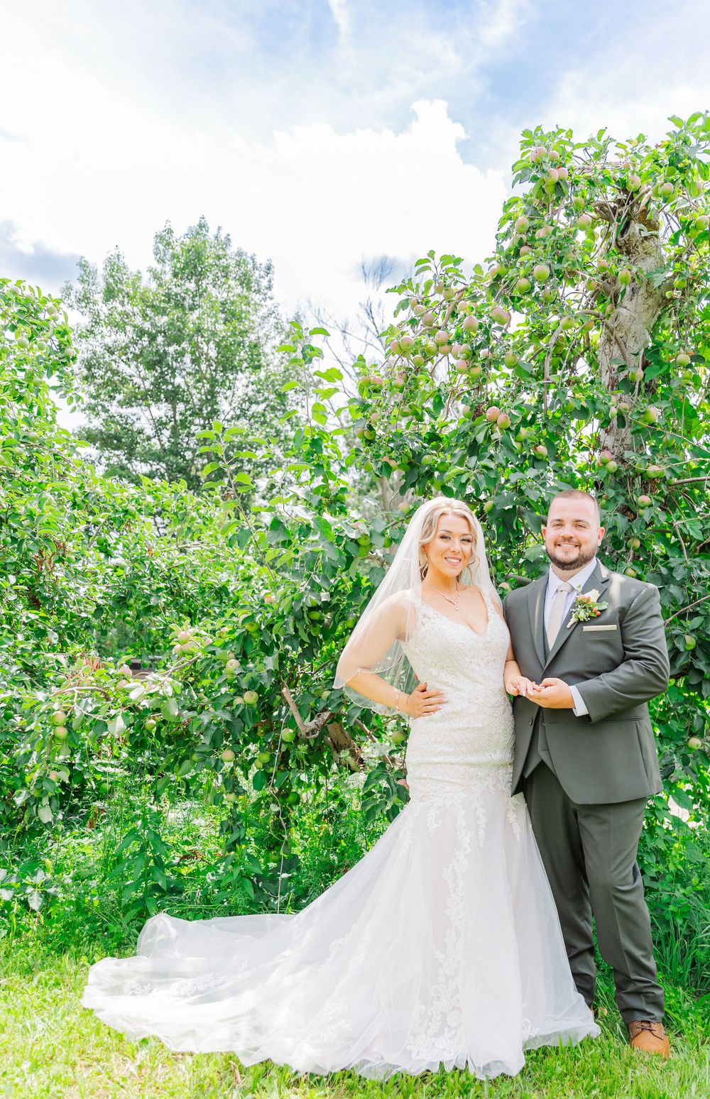 Wedding couple poses in front of blooming garden on bright summer day.