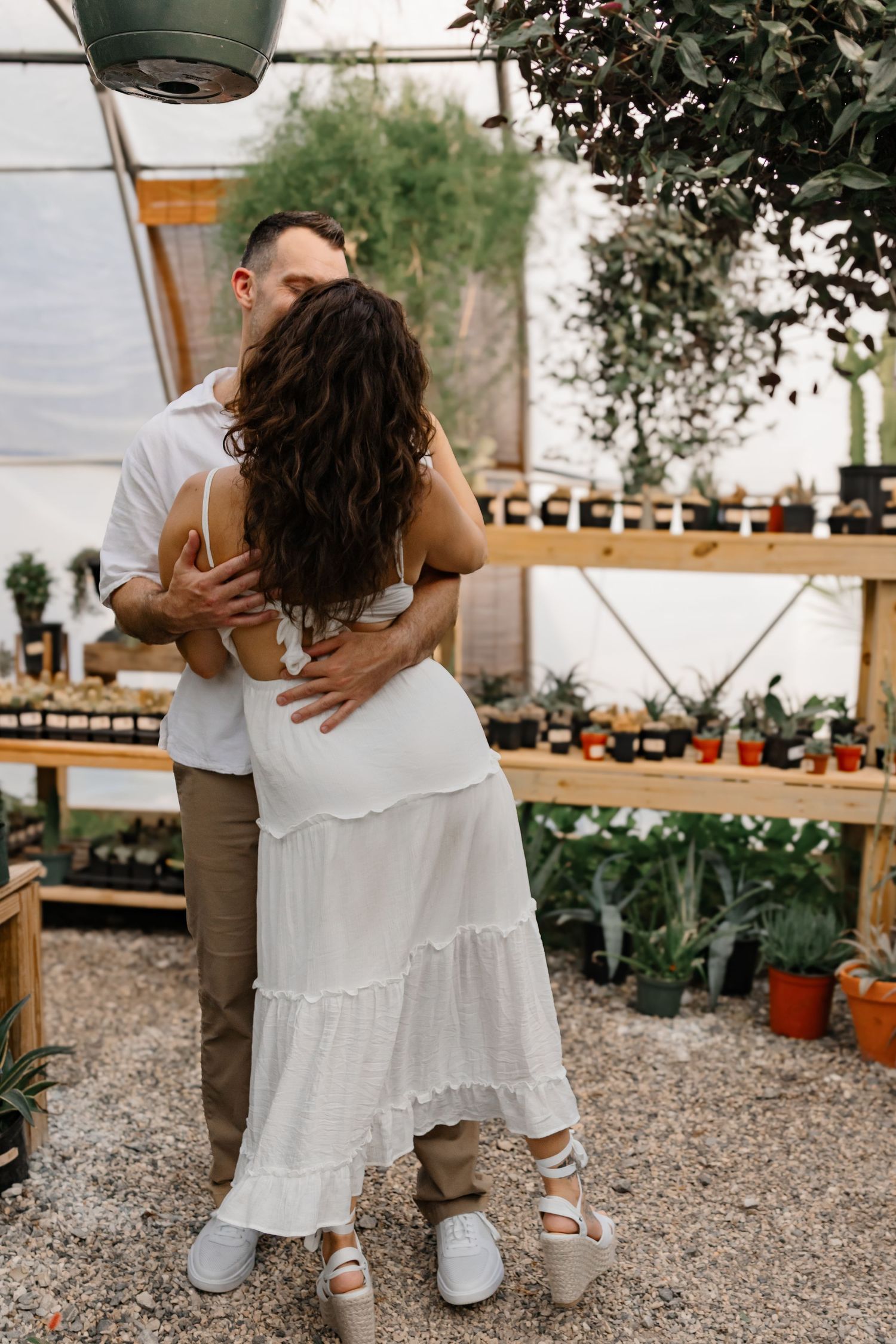 Intimate moment between couple embracing in plant-filled greenhouse.