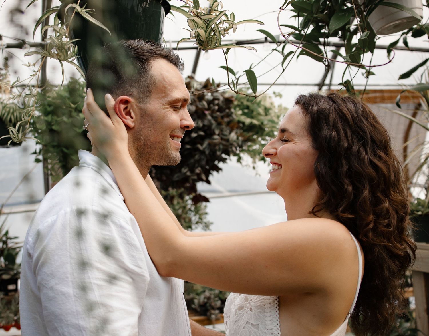 Couple sharing intimate moment among greenhouse plants and natural lighting.