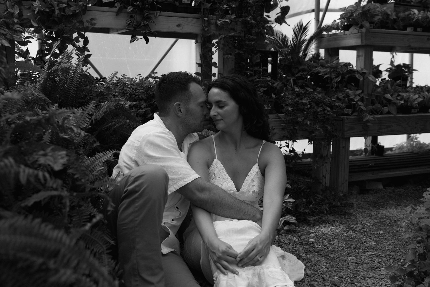 Black and white portrait of couple embracing in greenhouse setting.