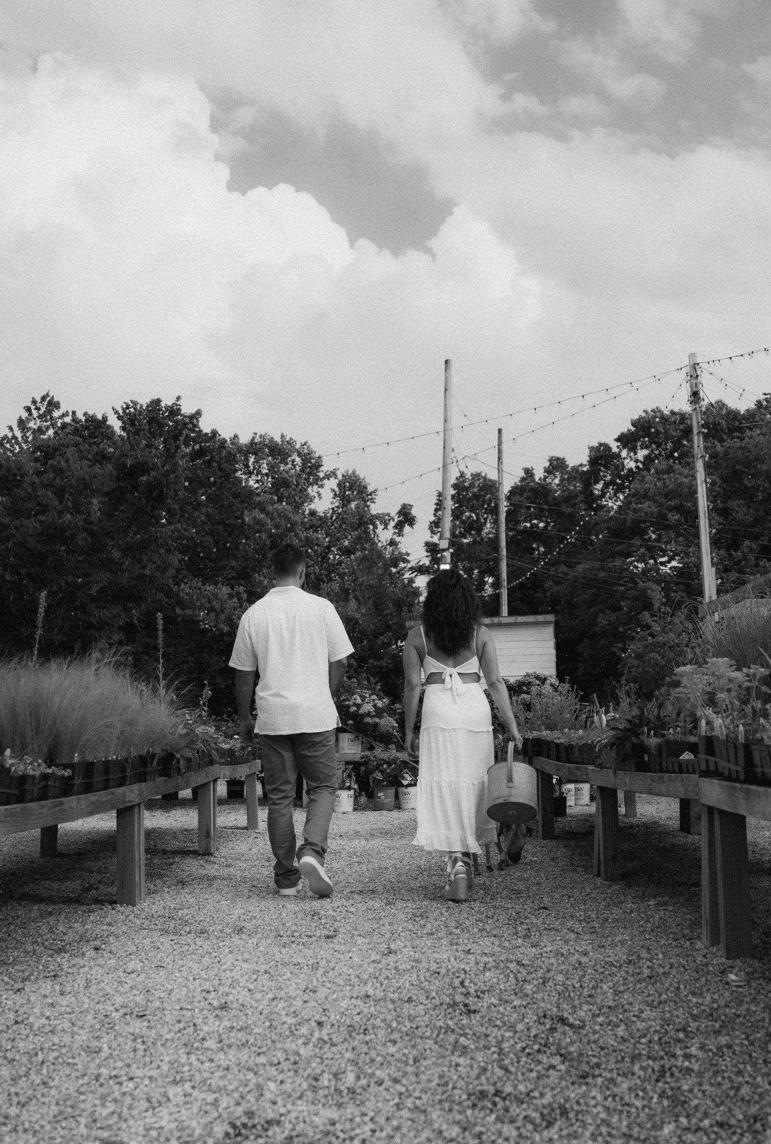 A couple walks together on a gravel path through a garden nursery on a cloudy day.