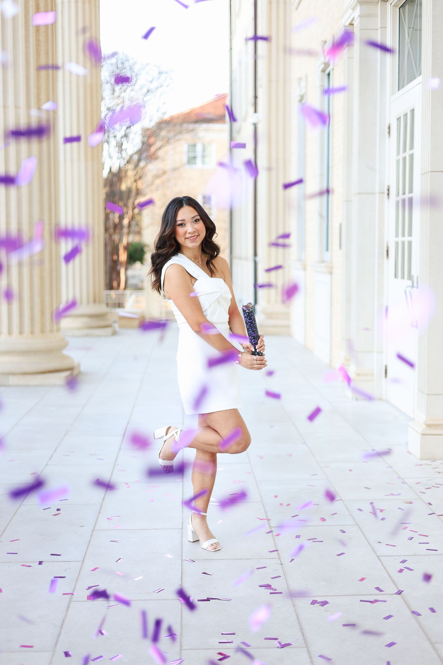 Celebratory graduation photo with purple confetti falling in front of columned building.