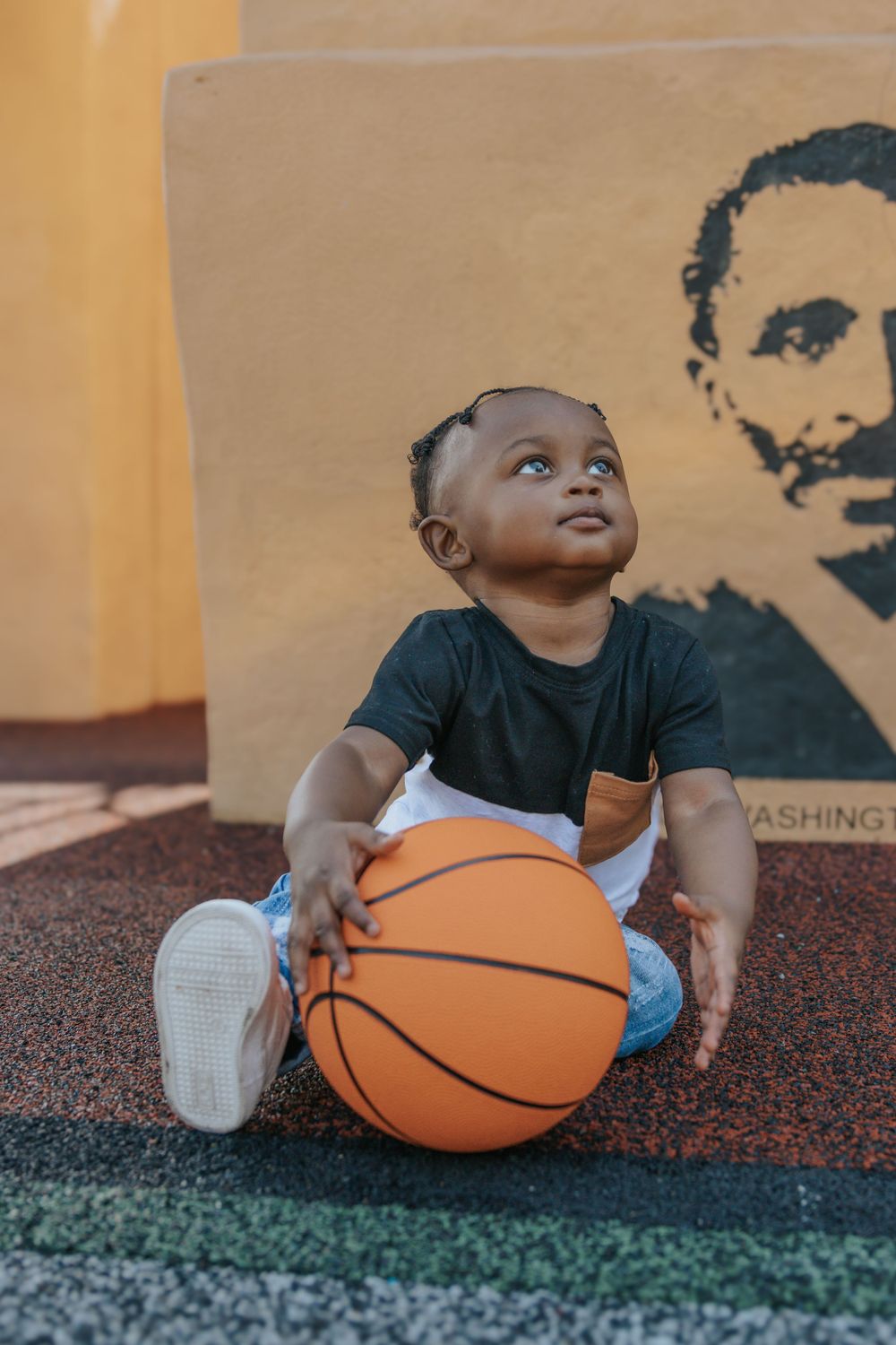 A child sits with a basketball near a wall featuring artistic silhouettes.