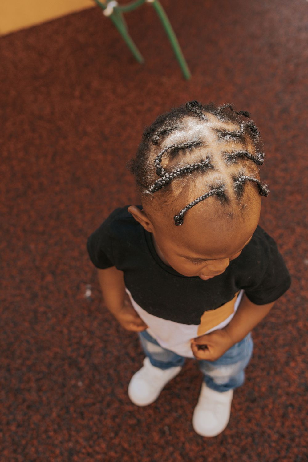 A child in a black and white outfit shows off intricate braided hairstyle from above.