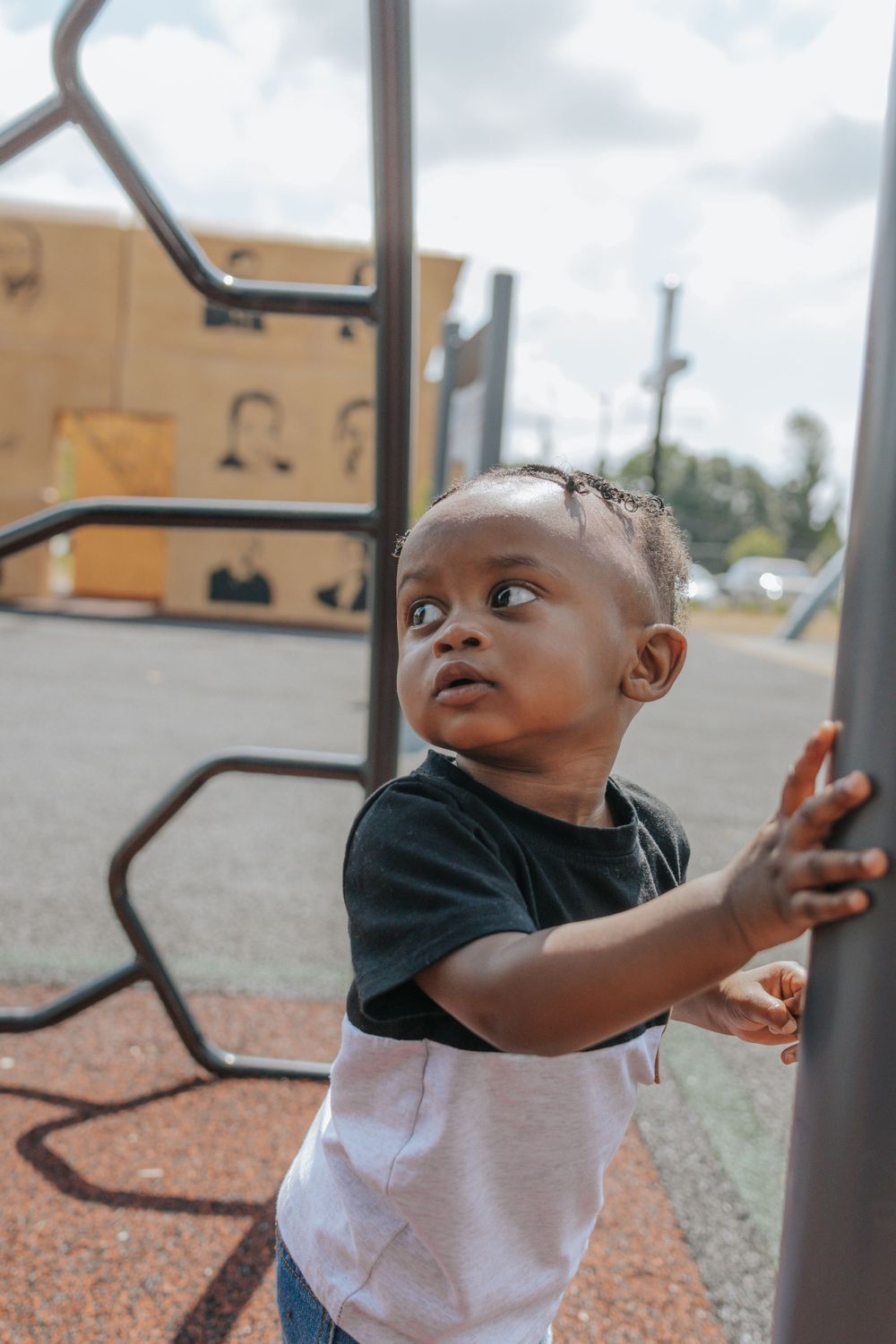 A child reaches for playground equipment while wearing a black and white outfit.