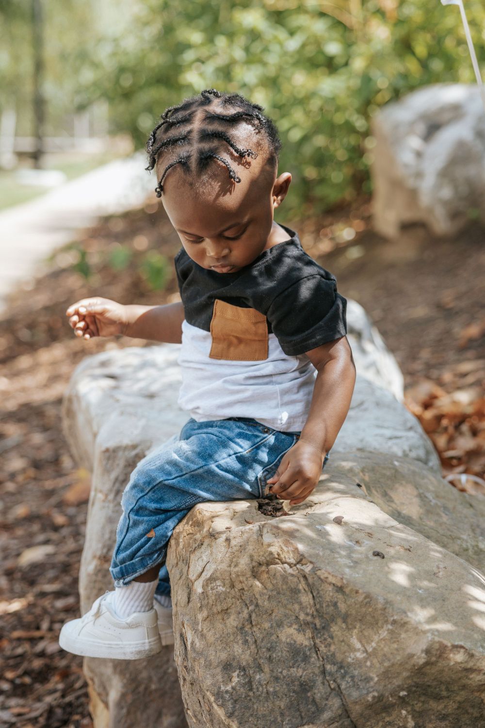 A small child climbs on a large rock while wearing a two-tone shirt and distressed jeans.