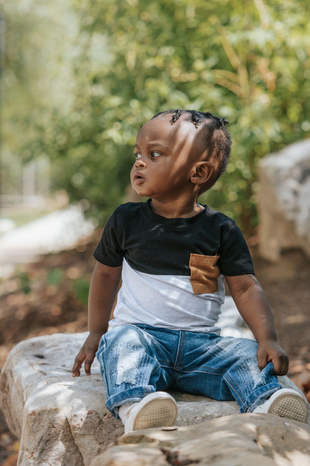 Toddler in black and white shirt sitting on rocks outdoors with natural background.