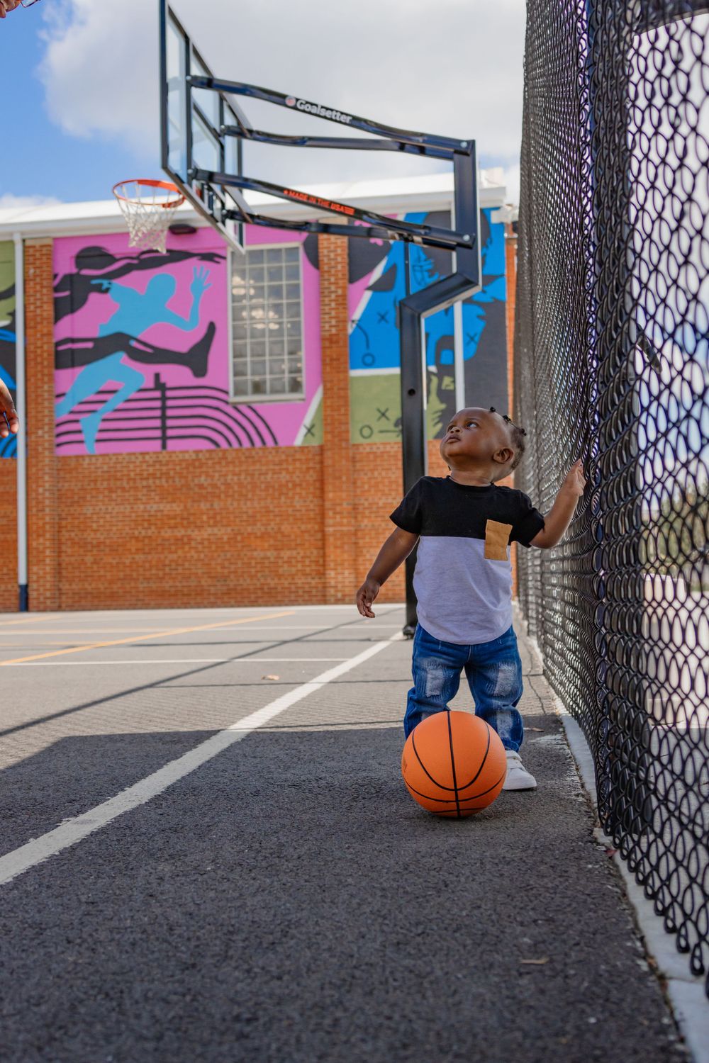 Small child standing near basketball hoop with ball on outdoor court.