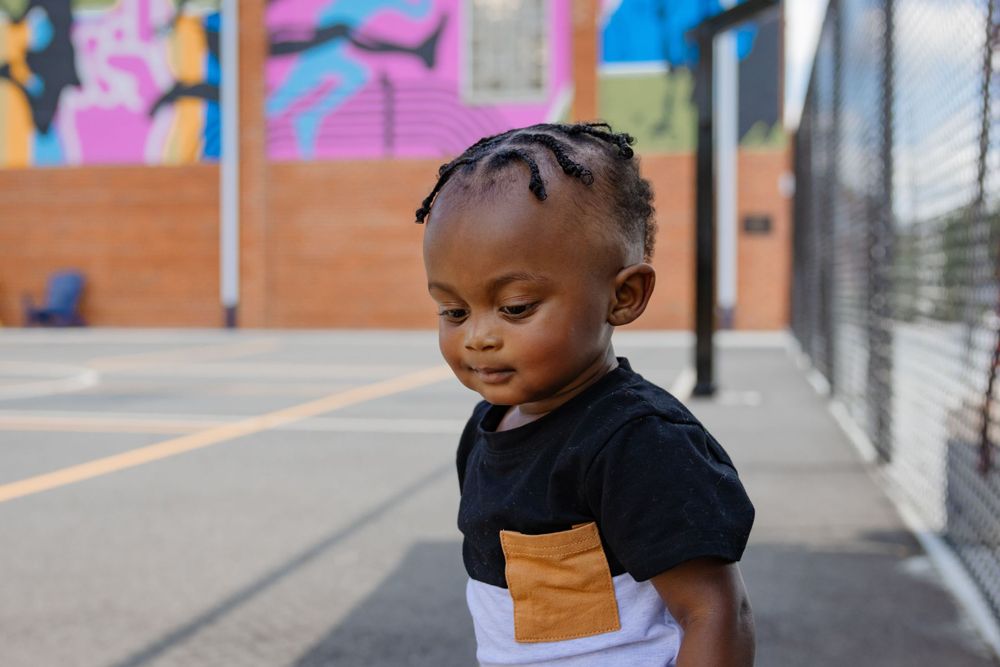 Toddler in two-tone shirt smiling while playing on basketball court.