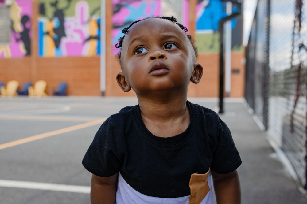 Young child looking up while standing on outdoor basketball court with mural wall.