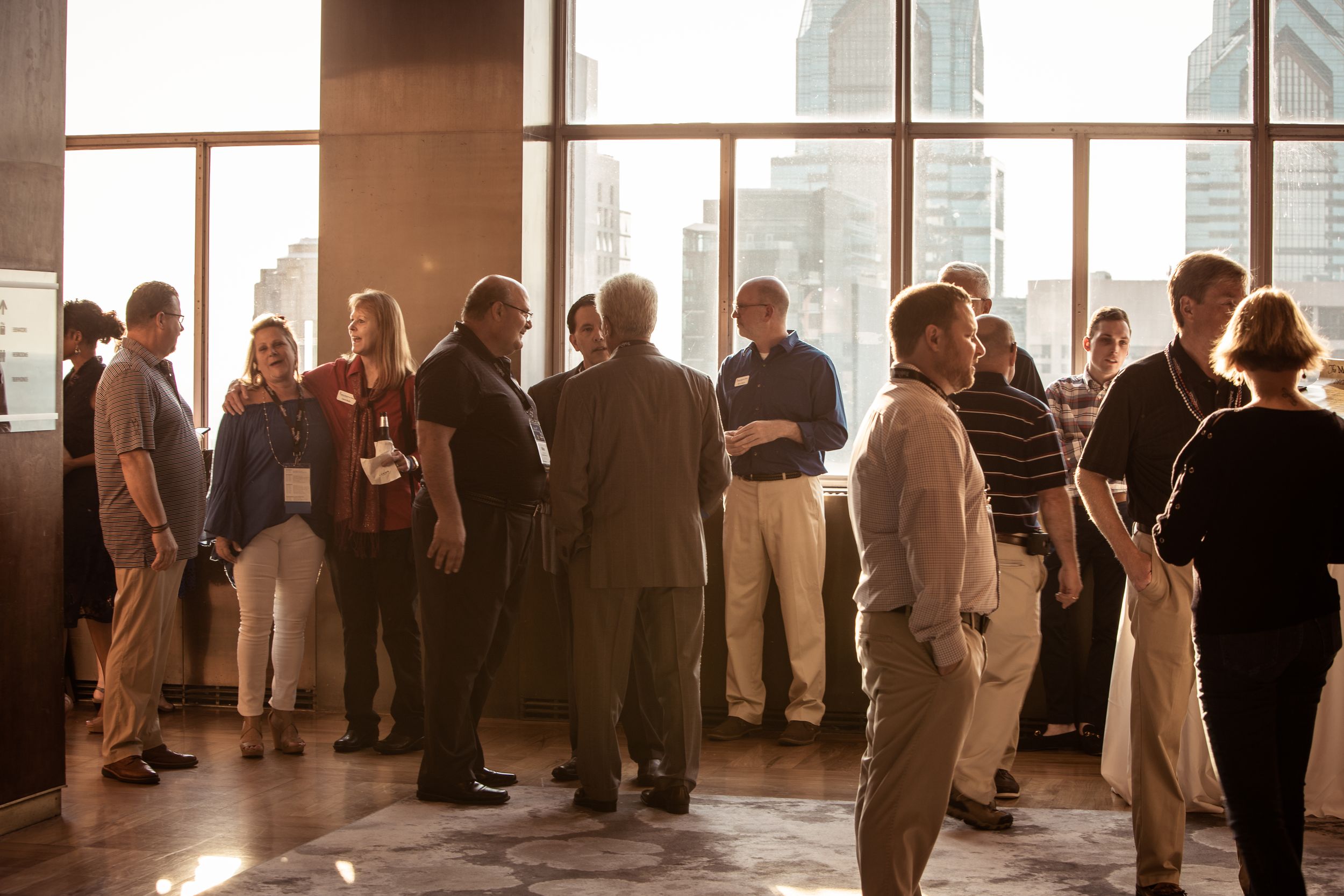 Business professionals networking at corporate event with city views through large windows.