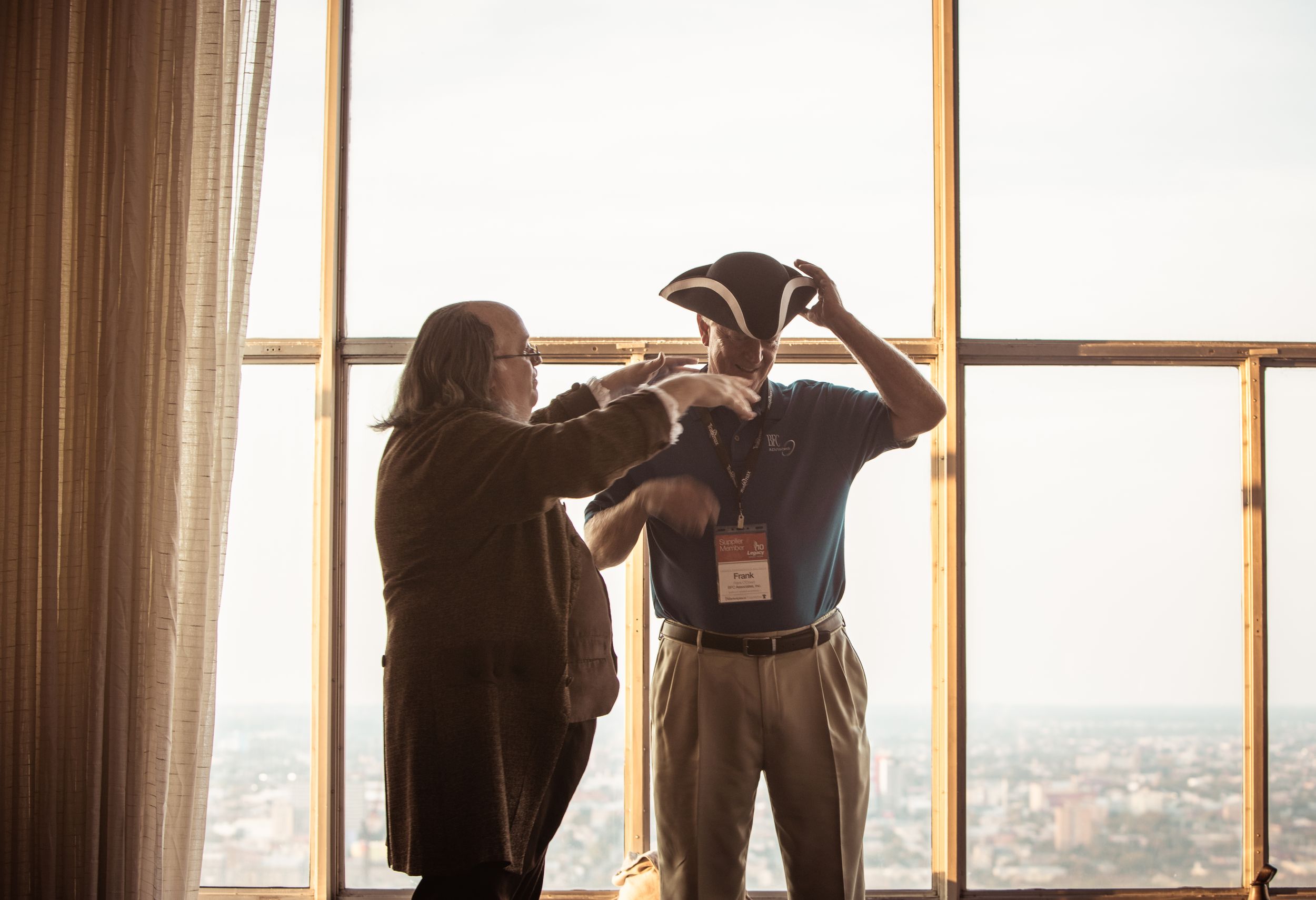 Two people looking through a large window in an office building with cityscape view.