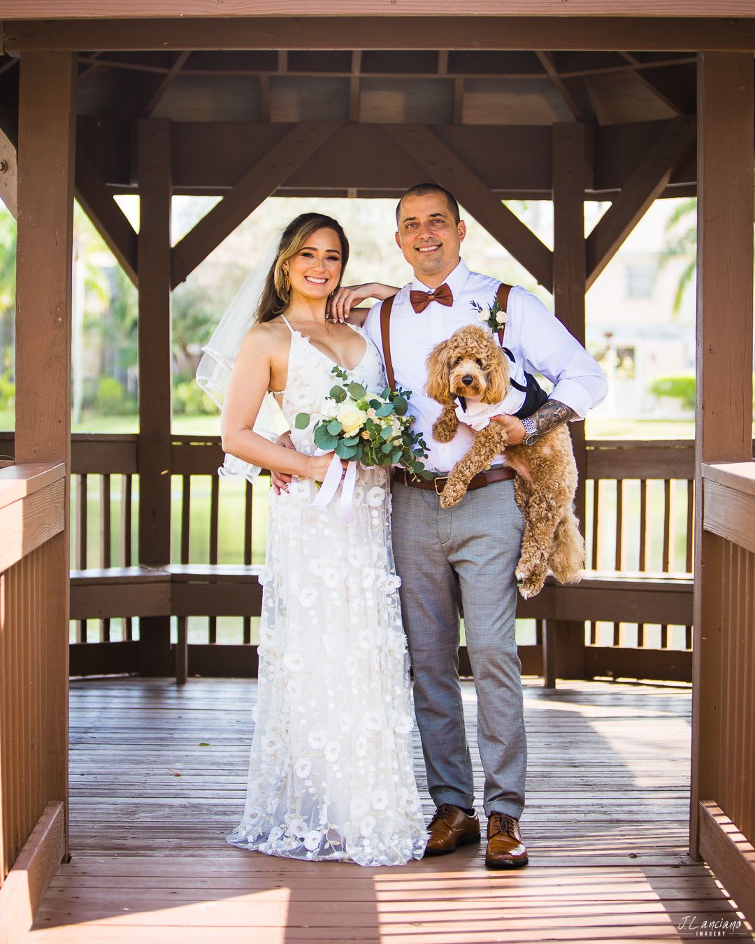 Couple poses with their dog in gazebo during wedding photoshoot.