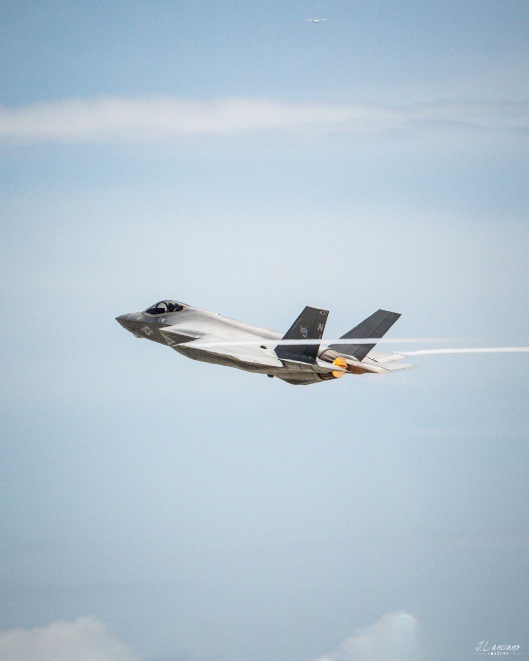 F-35 fighter jet soaring through bright blue sky with contrail visible behind.