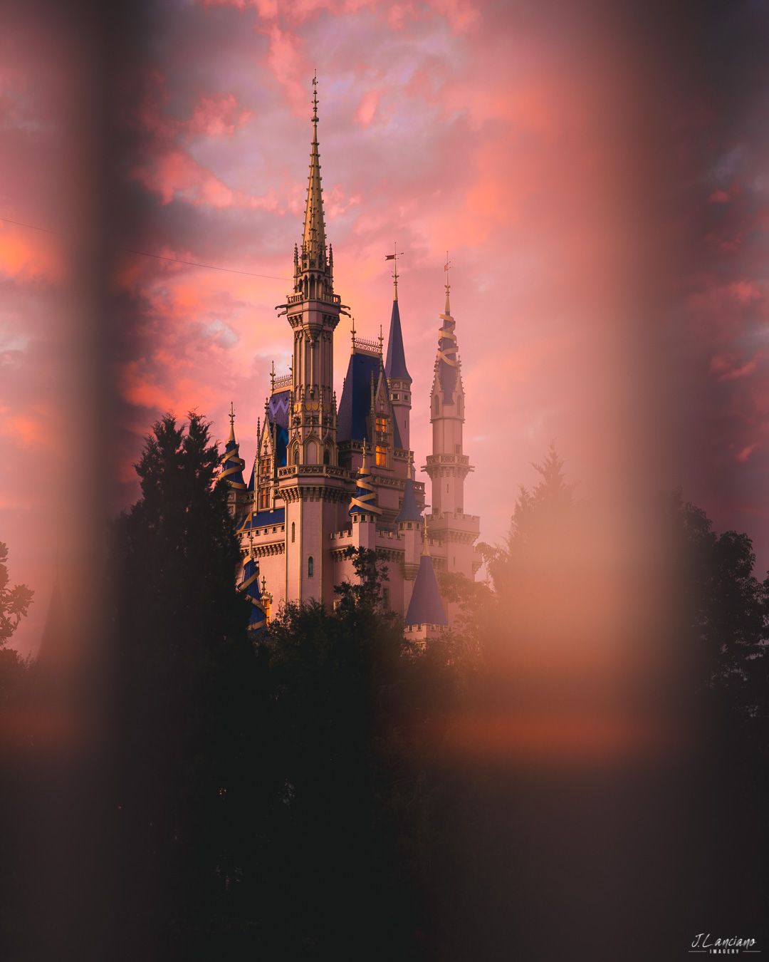 Disney castle spires silhouetted against dramatic pink and orange sunset sky.