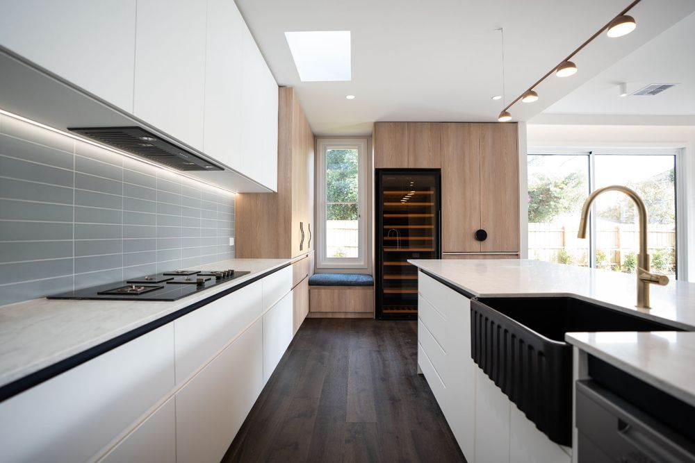 Contemporary white kitchen with black sink, wooden accents, and floor-to-ceiling cabinetry.
