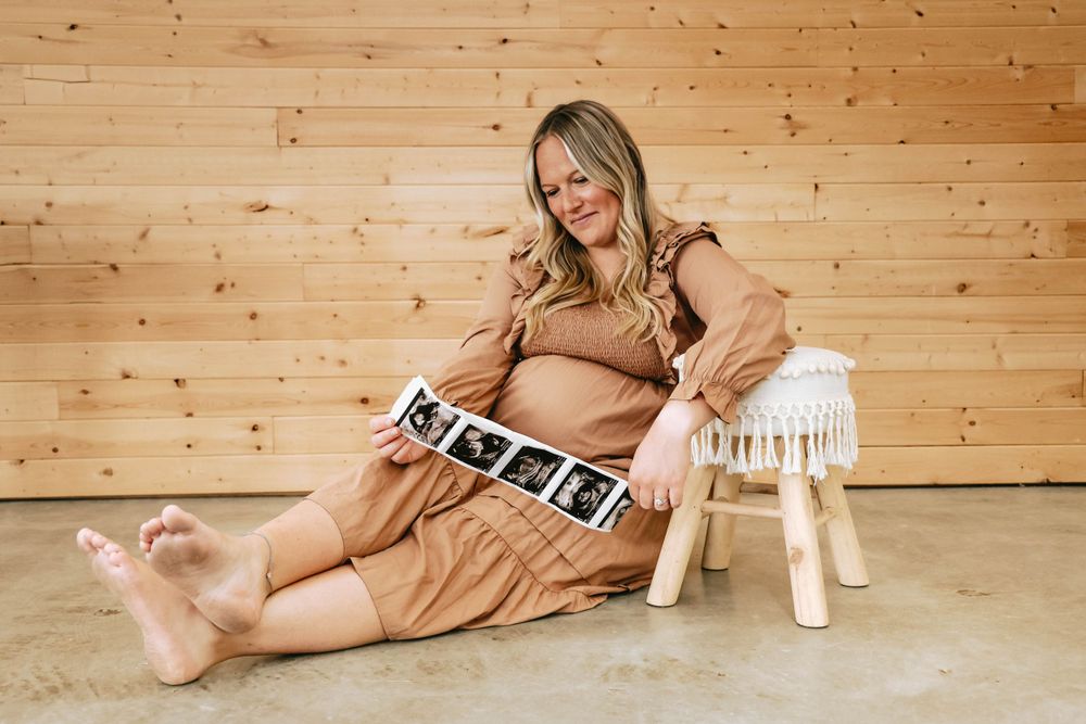 Maternity photo with ultrasound images displayed on wooden floor next to decorative white stool.