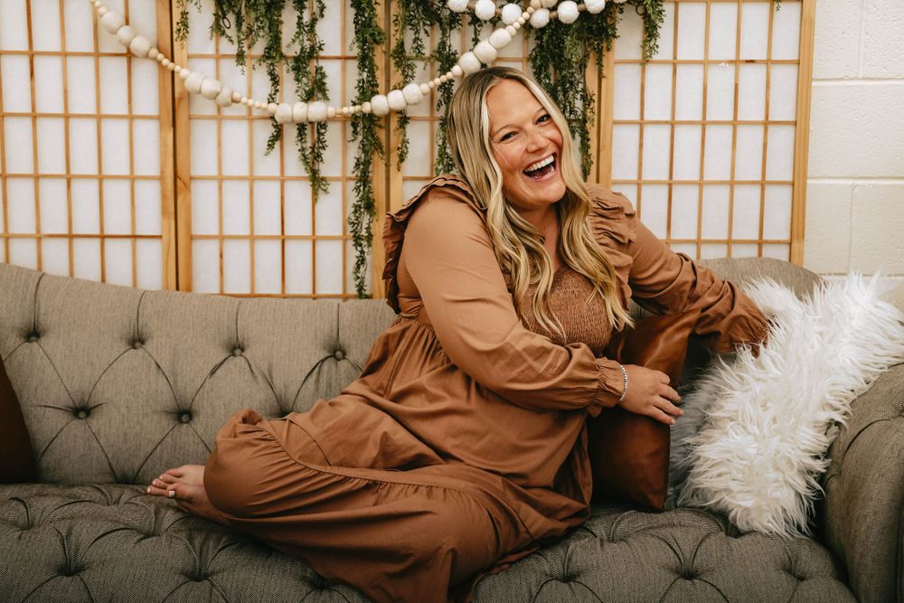 Maternity portrait on grey couch with floral backdrop and decorative lighting.