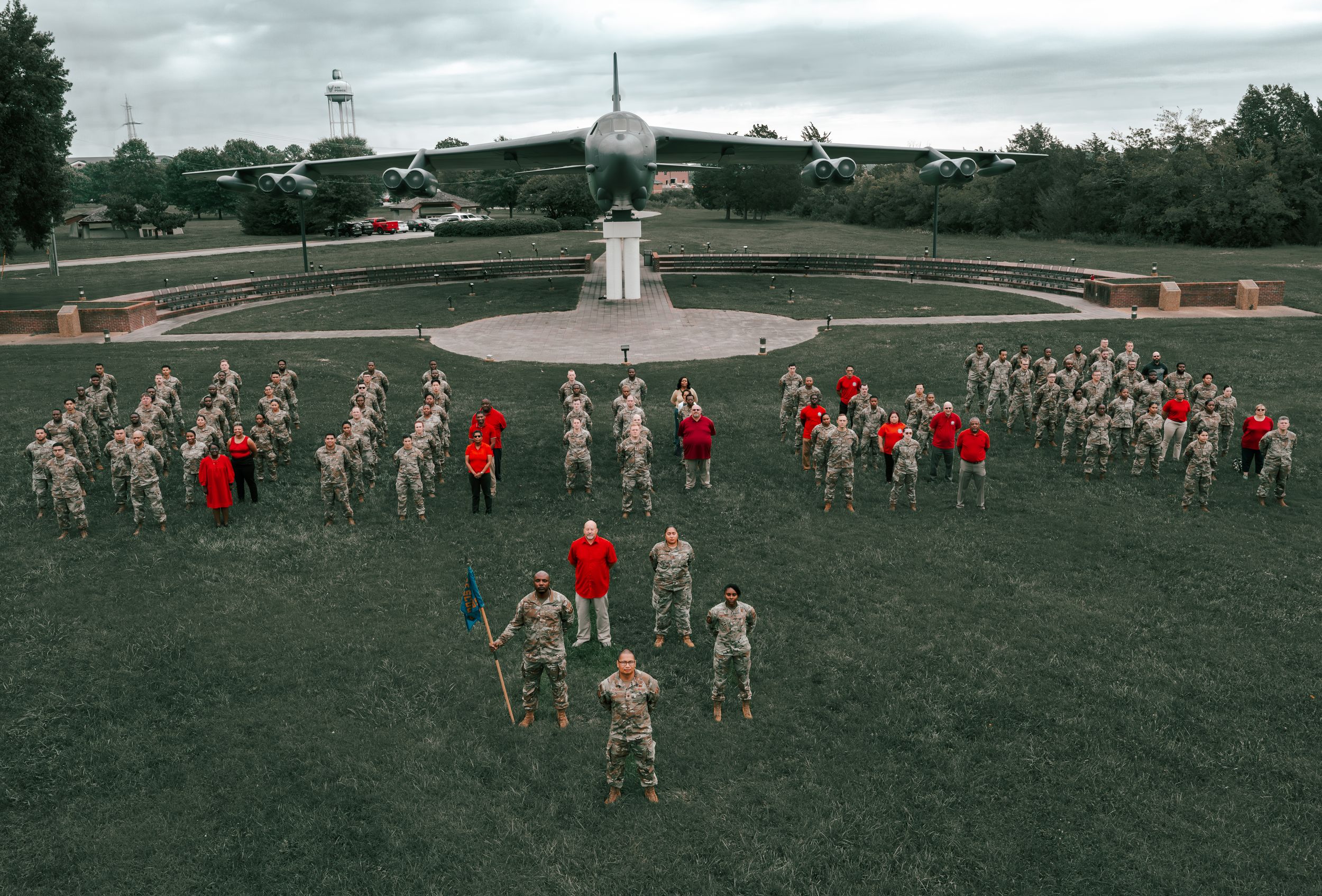 Aerial view of military formation with soldiers in khaki uniforms and red-uniformed leaders on a green parade ground.