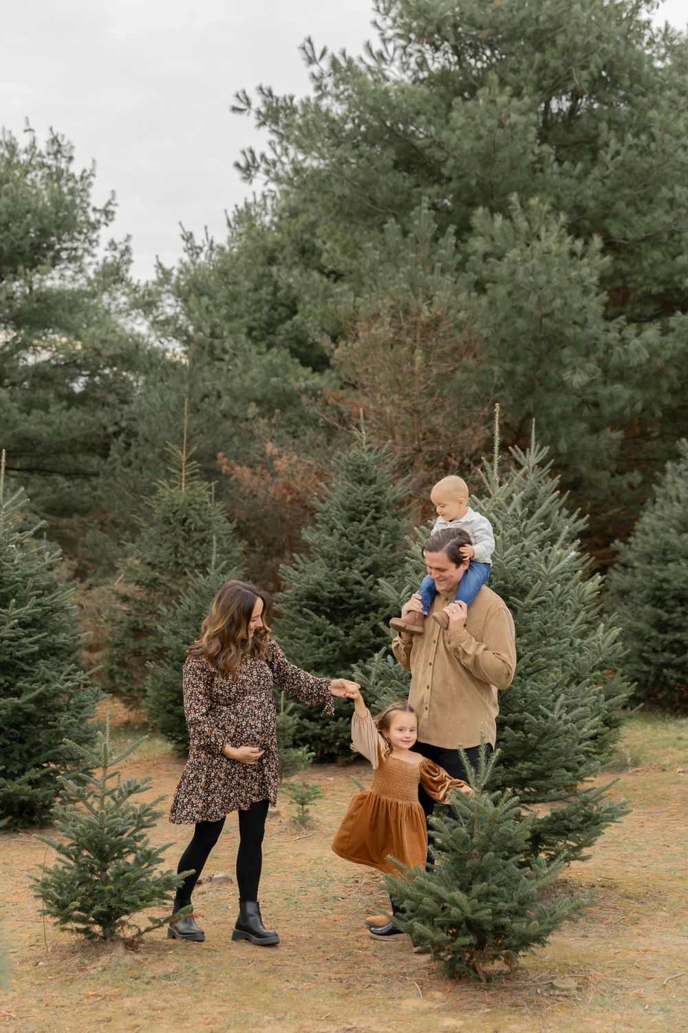 A family playing among evergreen trees at Addison oaks Christmas tree farm for a winter photoshoot