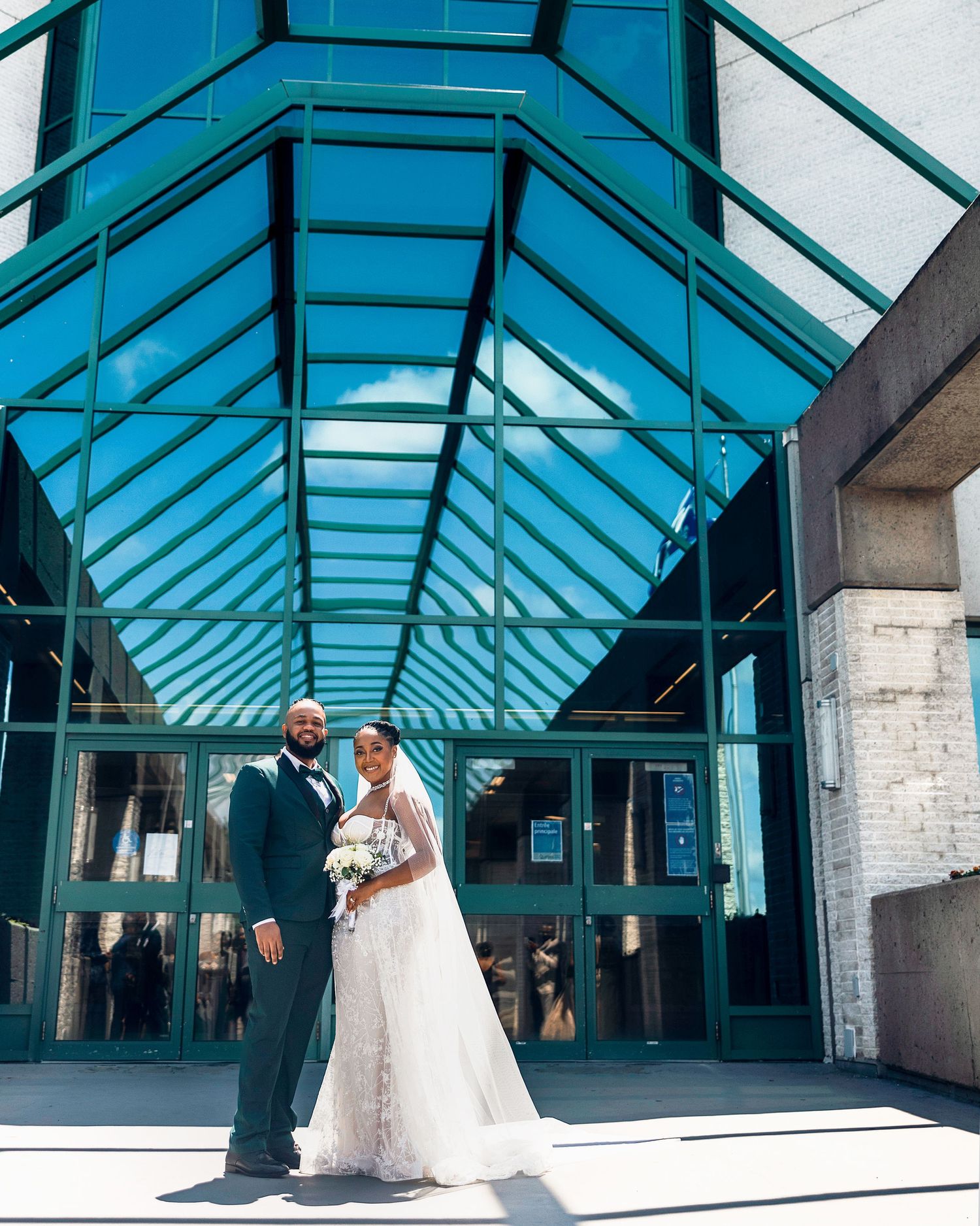 Elegant wedding photo under modern glass atrium with teal architectural details.