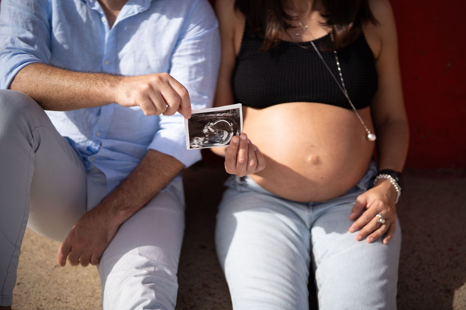 Couple holding ultrasound photo during waterfront maternity photoshoot.
