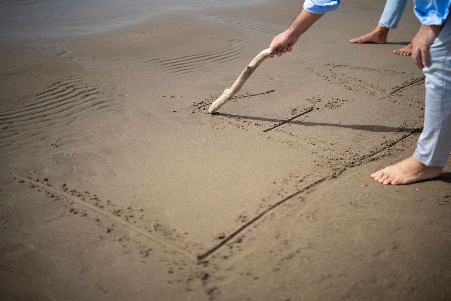 Someone draws a heart shape in the wet sand on a beach.