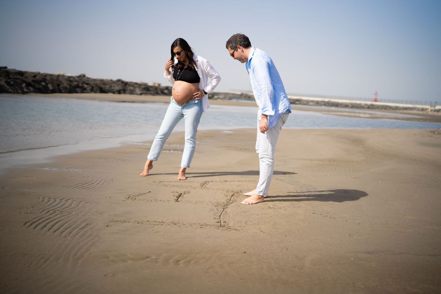 A couple playfully drawing in the sand on a sunny beach.