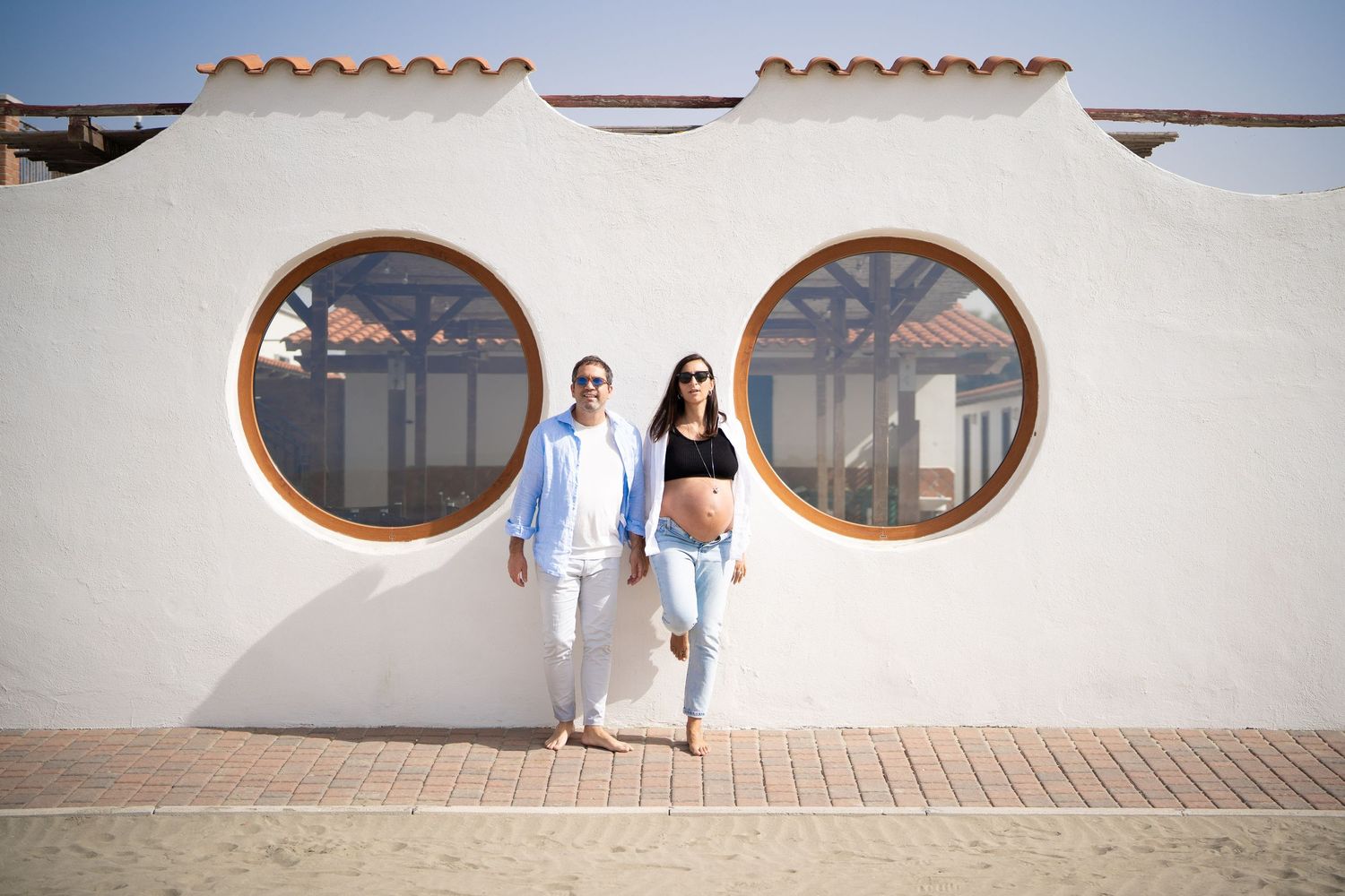 A couple poses in front of a white building with distinctive round windows.
