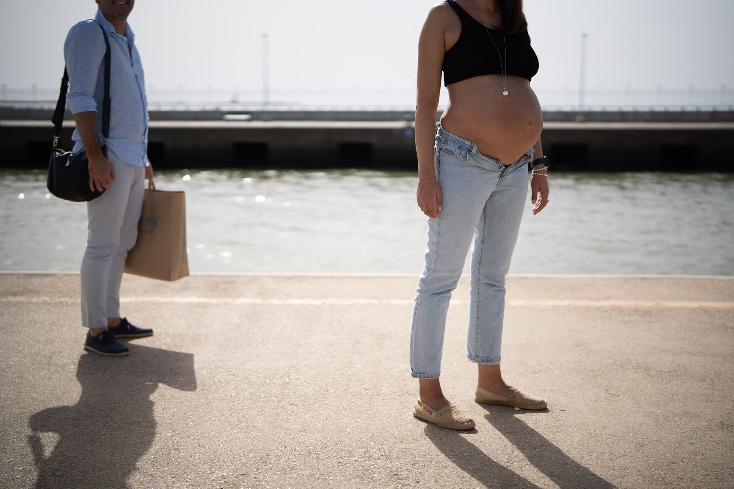 Casual maternity shoot showing couple's shadows on sunlit pier.