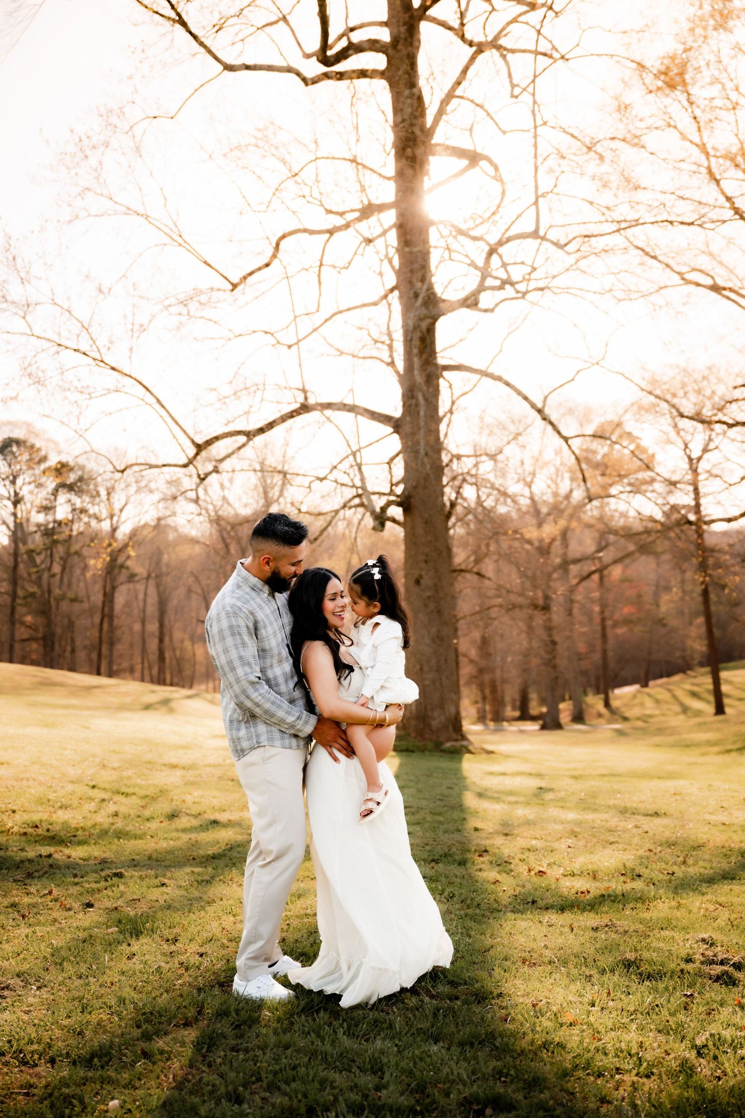 A romantic couple dances in a sunlit field with bare trees in the background during golden hour.