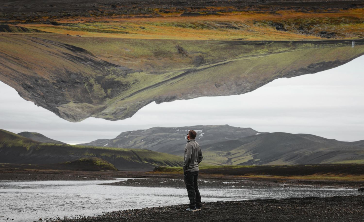 Hiker stands beside a large snow patch in a dramatic volcanic landscape during summer in Iceland.
