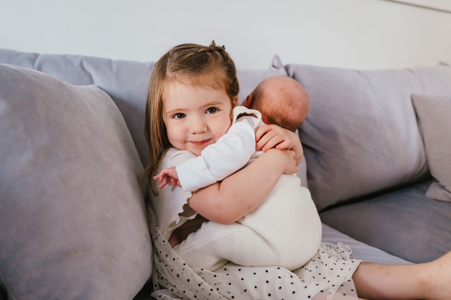 A child sitting on a gray couch holds a baby.