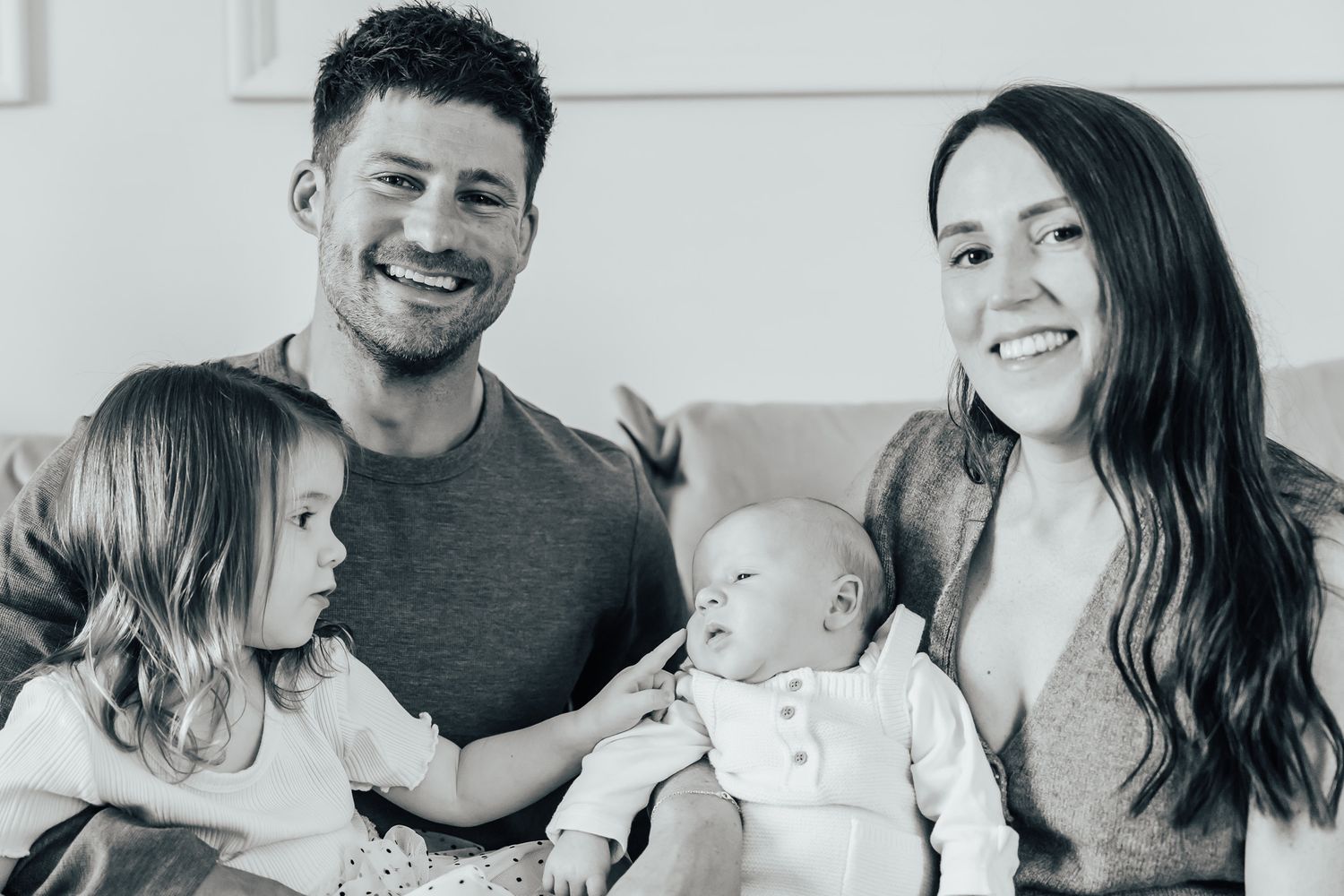 A happy family sitting together on a couch in black and white.