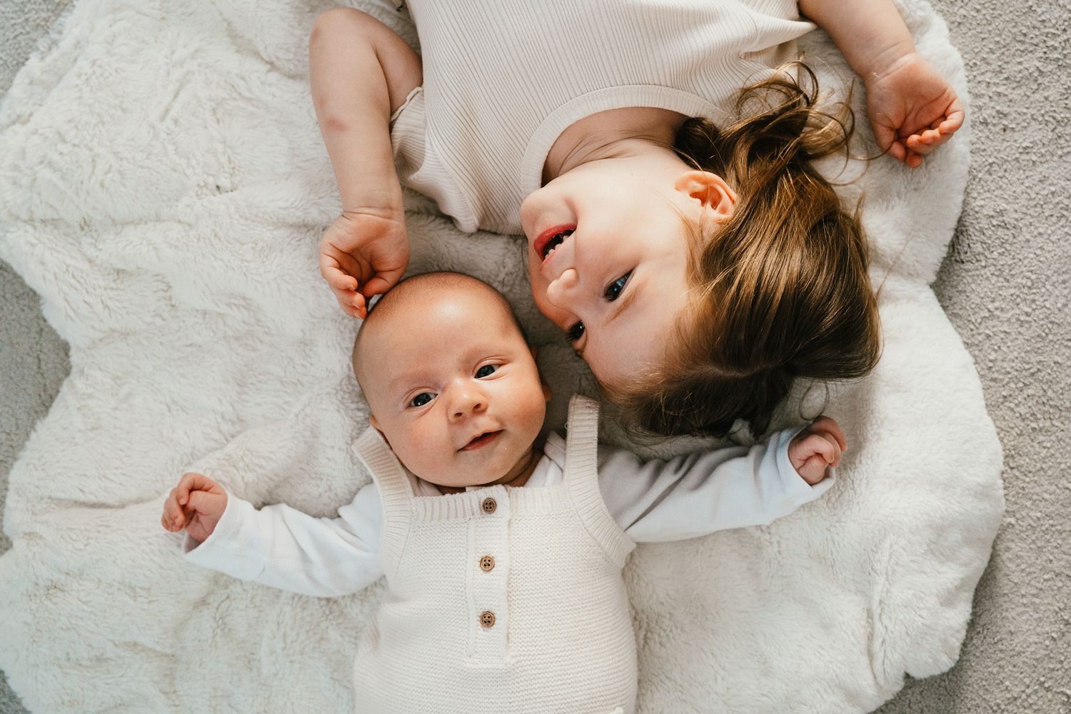 Two children lying on a white blanket together.