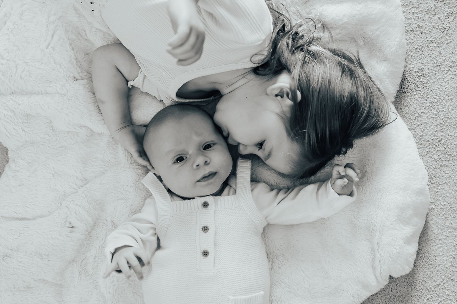 Two children lying on white fabric in a black and white photo.