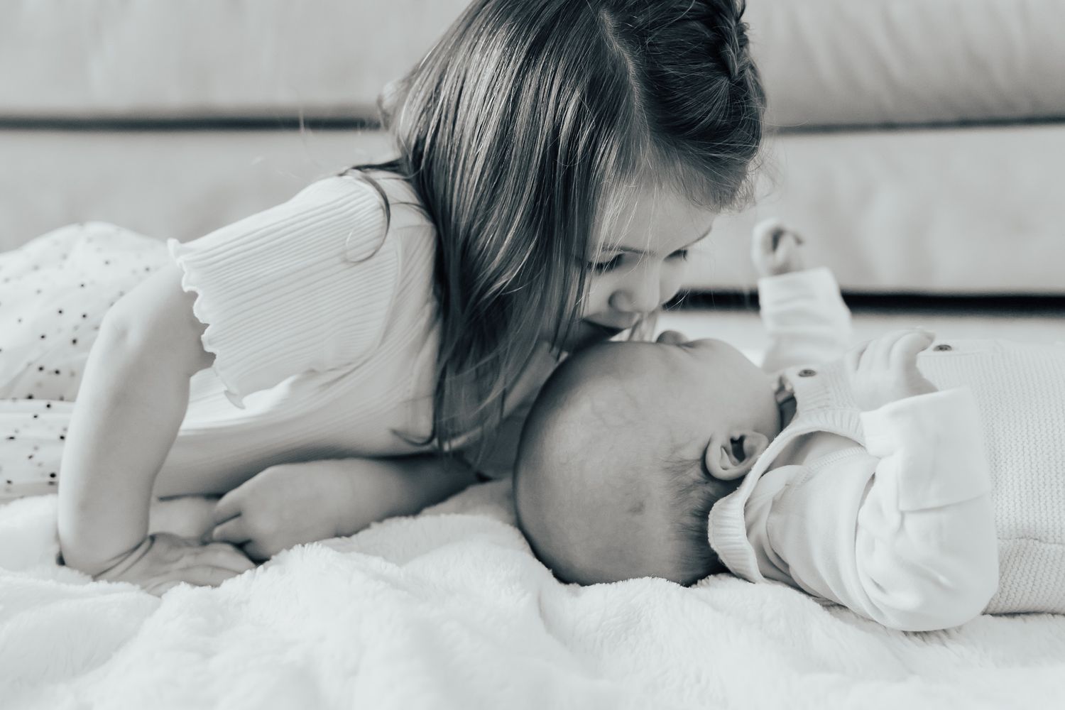 Two children sharing a tender moment on white bedding.