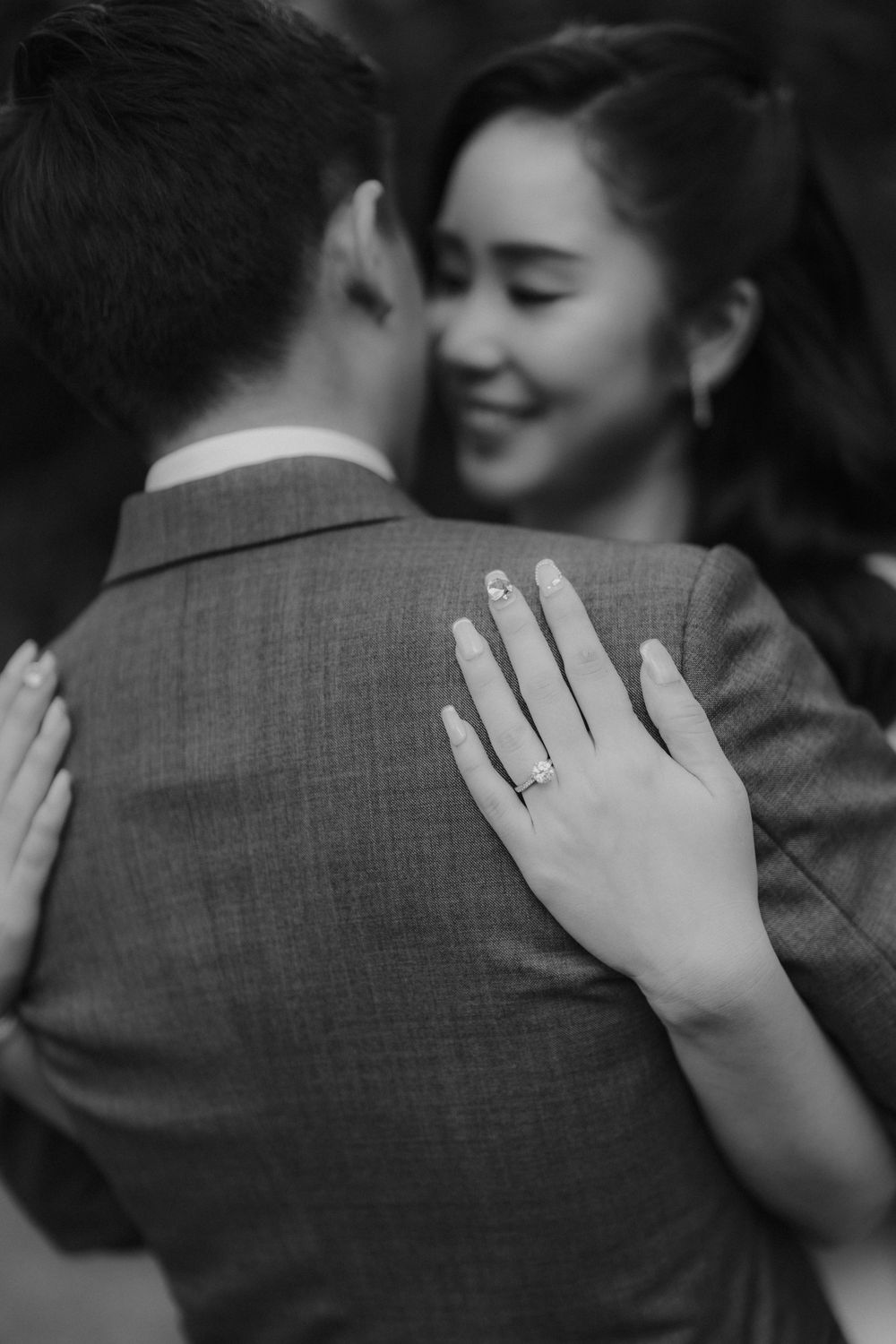 A black and white photo showing hands with an engagement ring during an embrace.