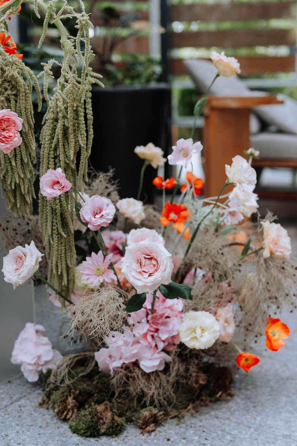 Modern floral arrangement featuring pink roses, orange blooms, and cascading dried elements.