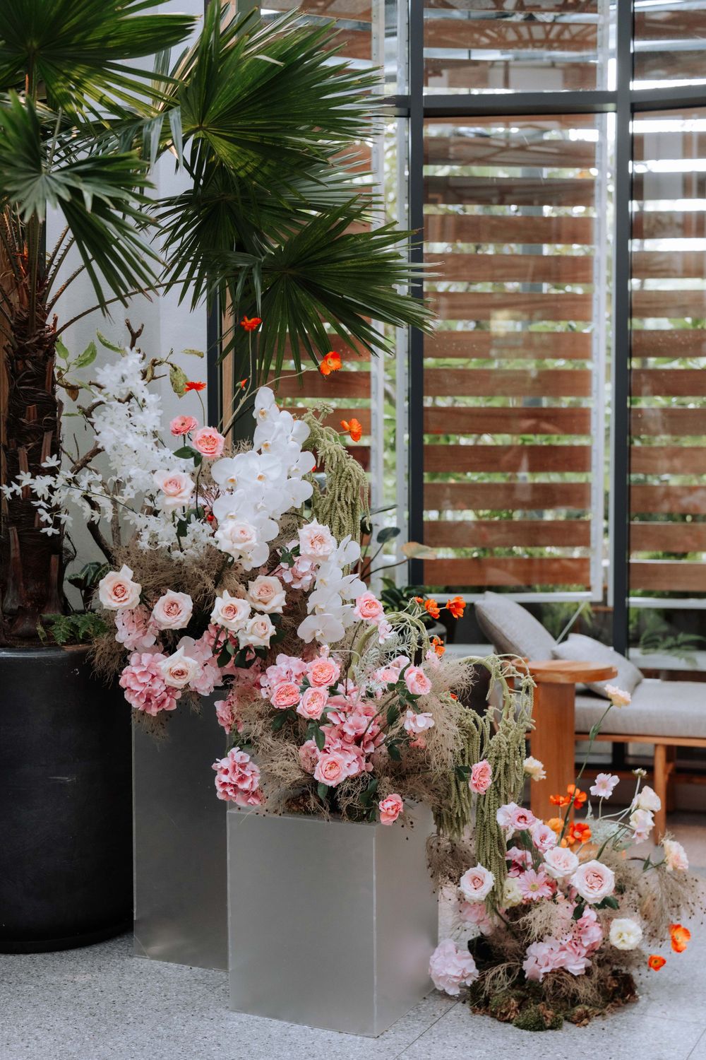 Tropical garden wedding decor with palm trees and pink floral arrangements in modern planters.