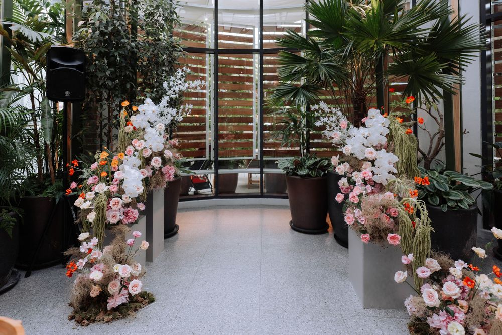 Wedding ceremony aisle decorated with pink floral arches in a modern greenhouse setting.
