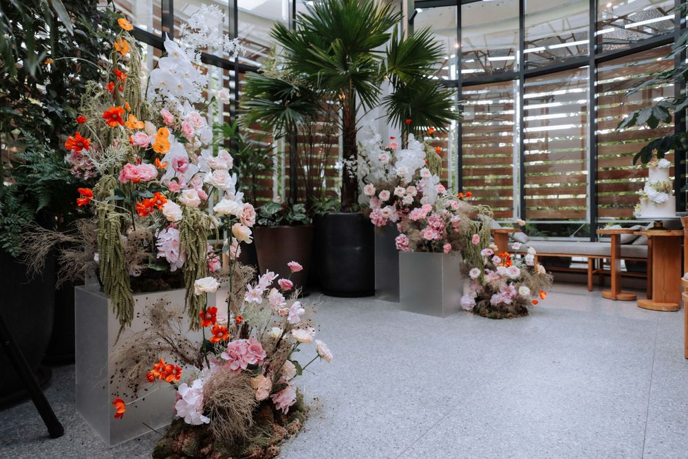 Elegant floral arrangements with orchids and roses decorate a modern indoor space with window blinds.