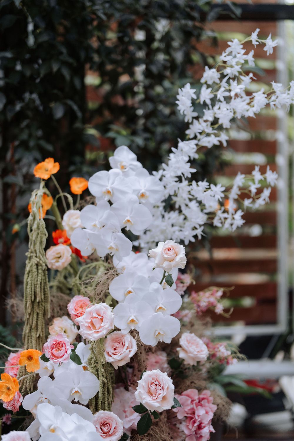 Close-up of white orchids and pink roses in an ornate floral arrangement against a brick wall.
