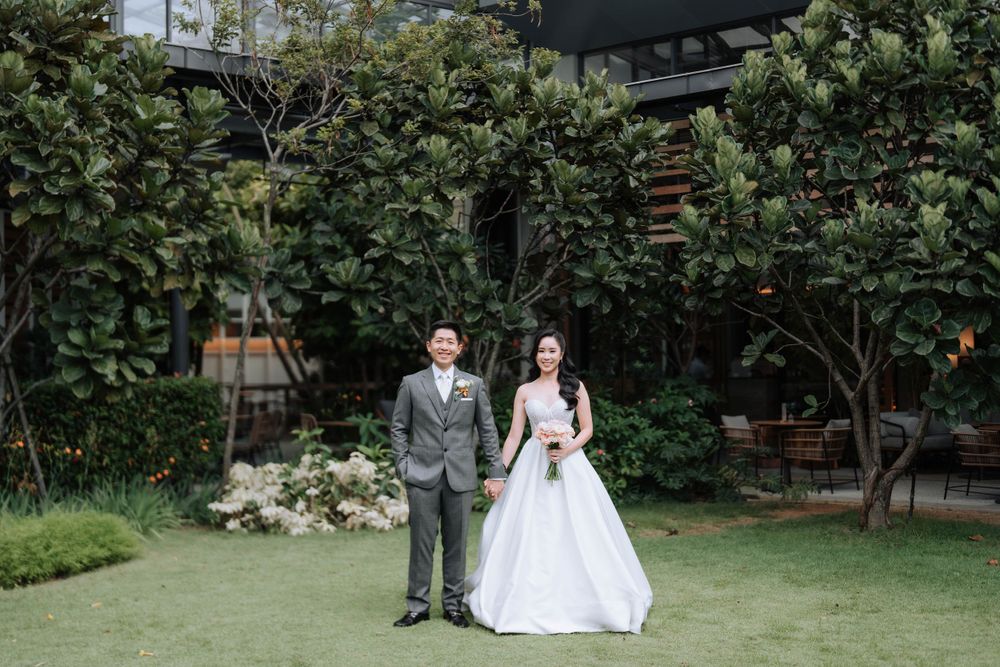 A wedding couple poses in a lush garden setting surrounded by greenery.