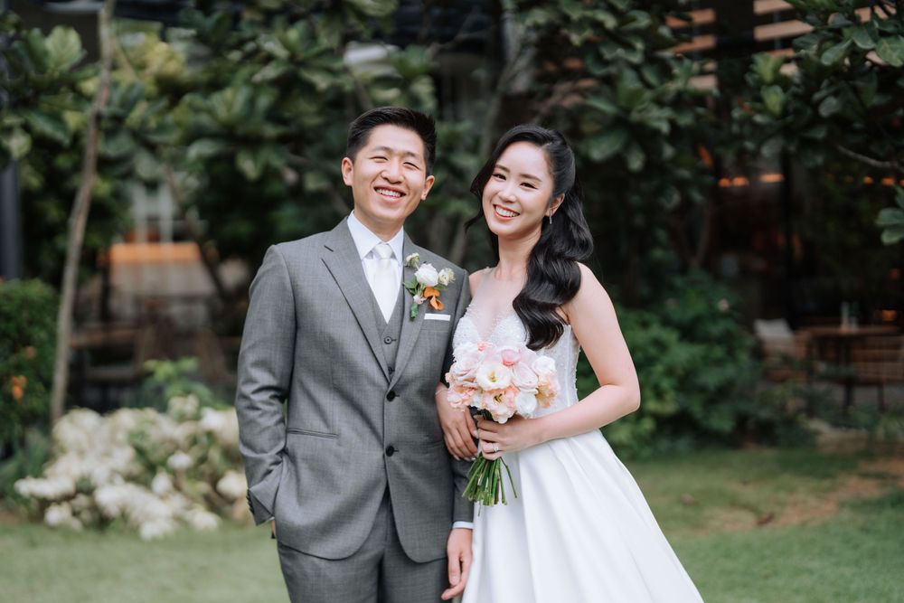 A wedding couple smiles brightly while posing in a garden setting.