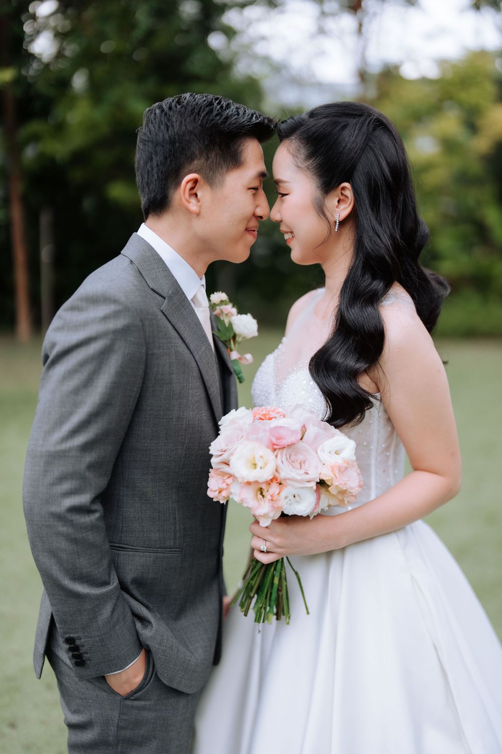 An intimate moment between newlyweds holding a pink rose bouquet in a garden setting.