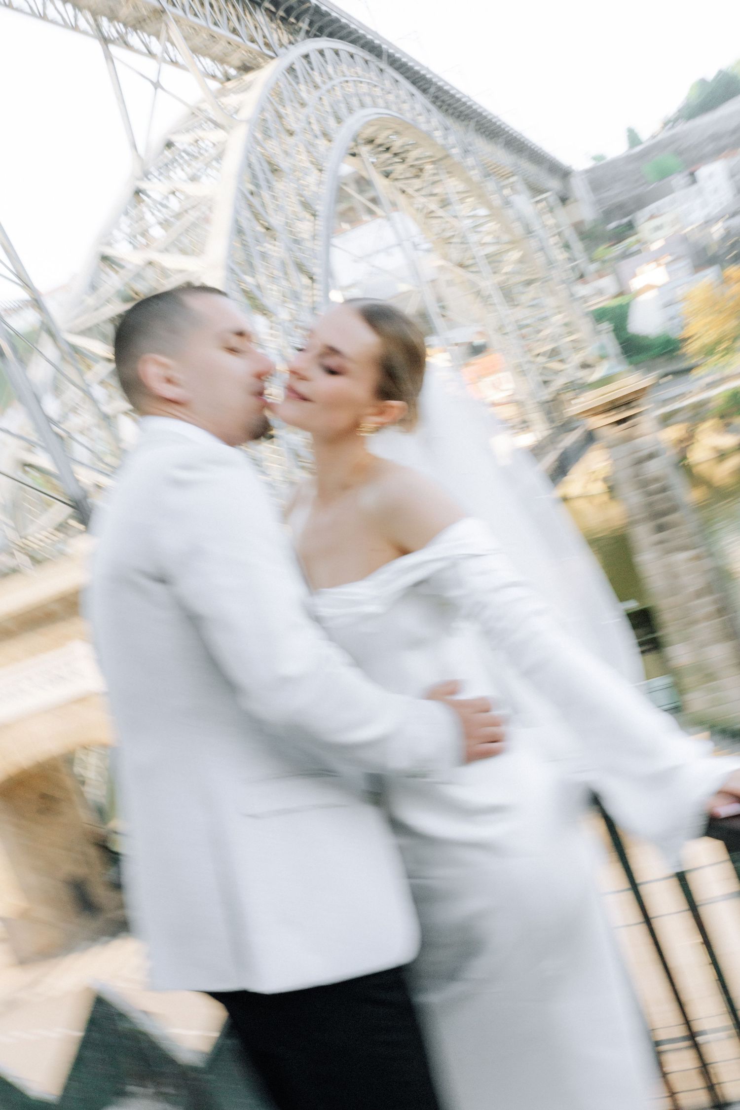 A couple embraces in front of a grand white stone church with ornate Gothic windows and architectural details.