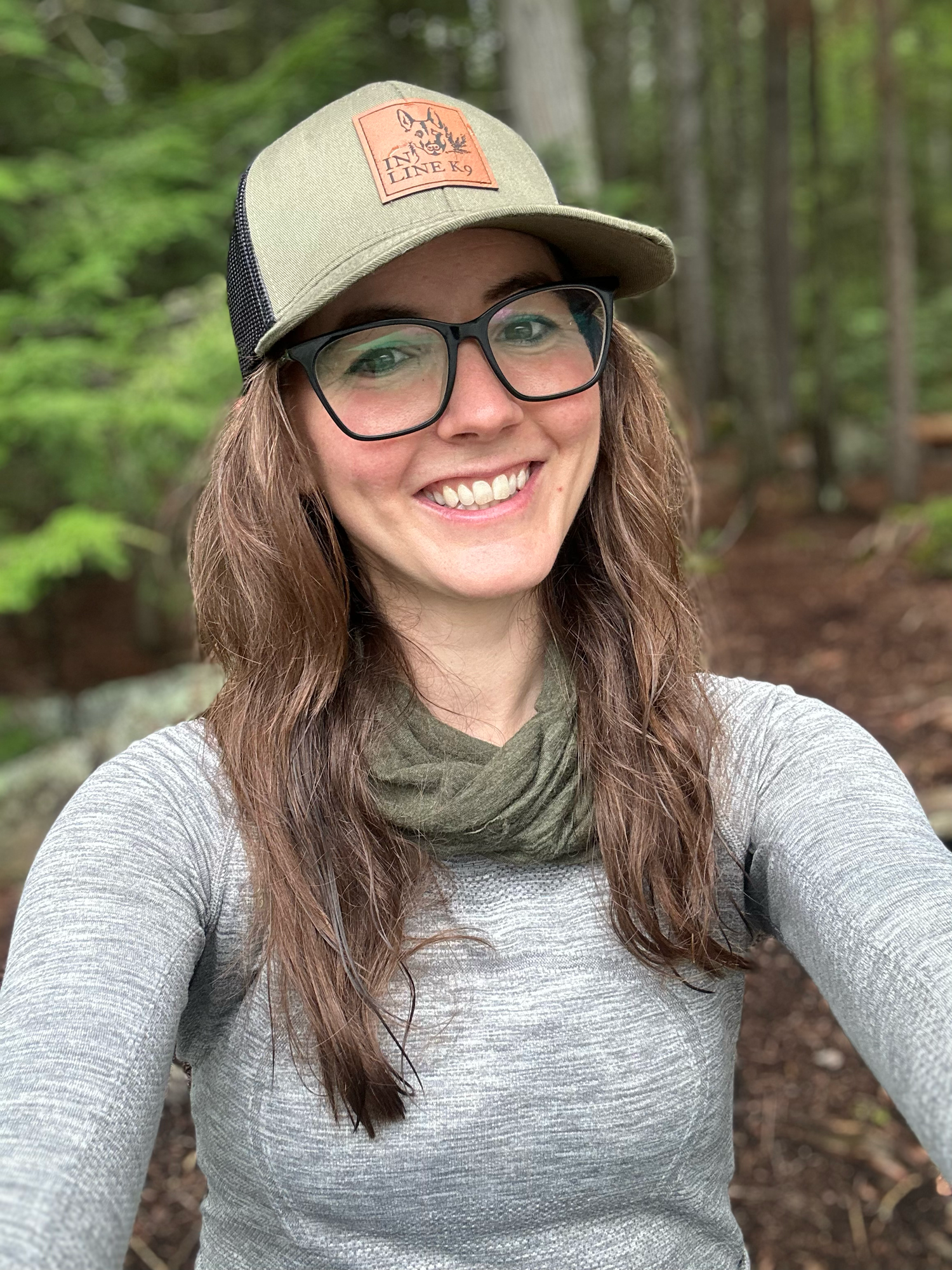 Someone wearing a grey shirt and baseball cap takes selfies in a forest setting.