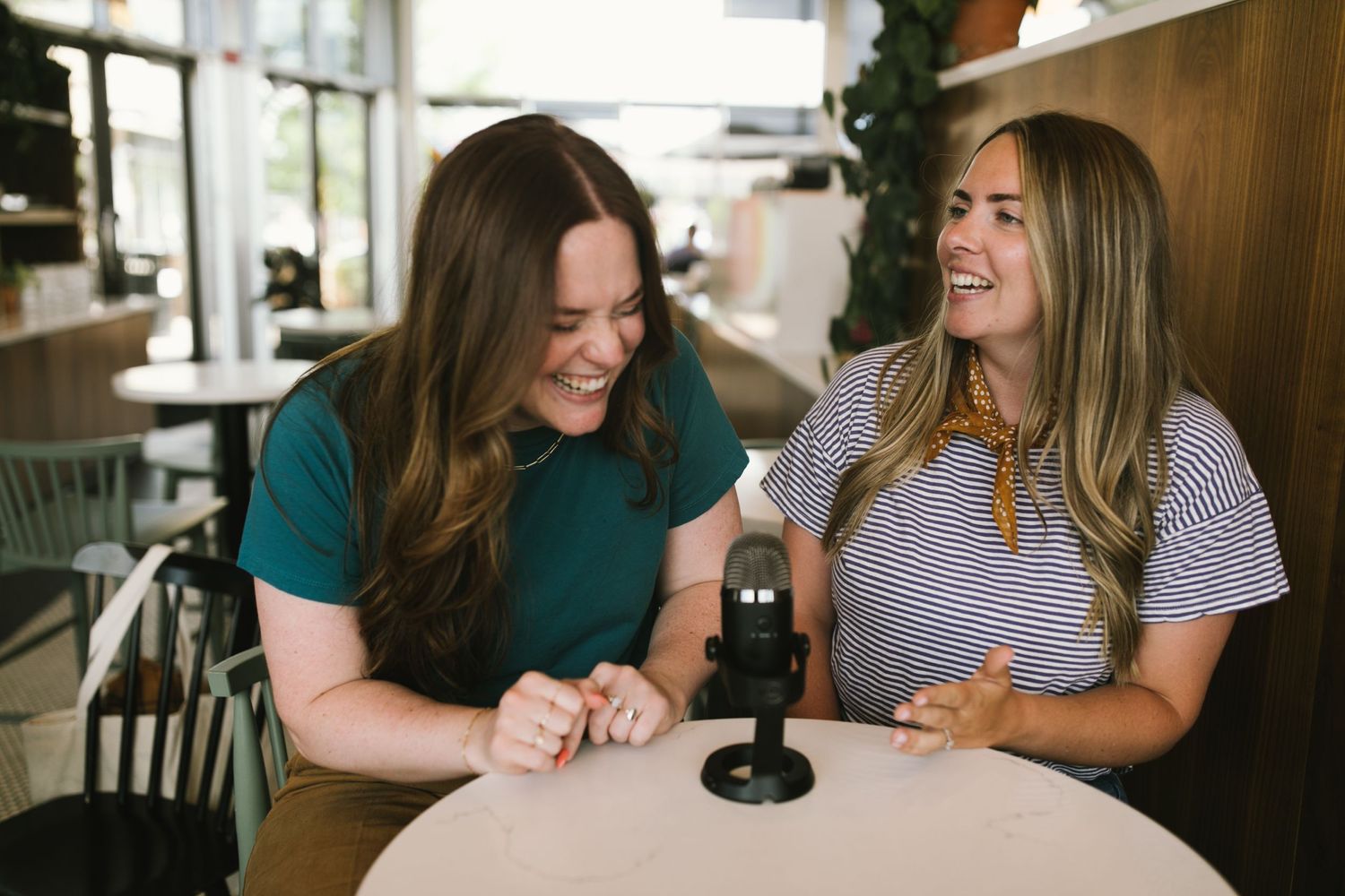Two friends share a laugh while sitting at a cafe table.